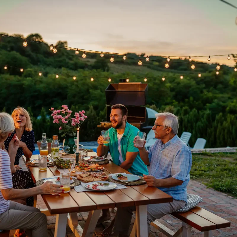 Una famiglia che cena in giardino al tramonto con tavola apparecchiata e atmosfera estiva